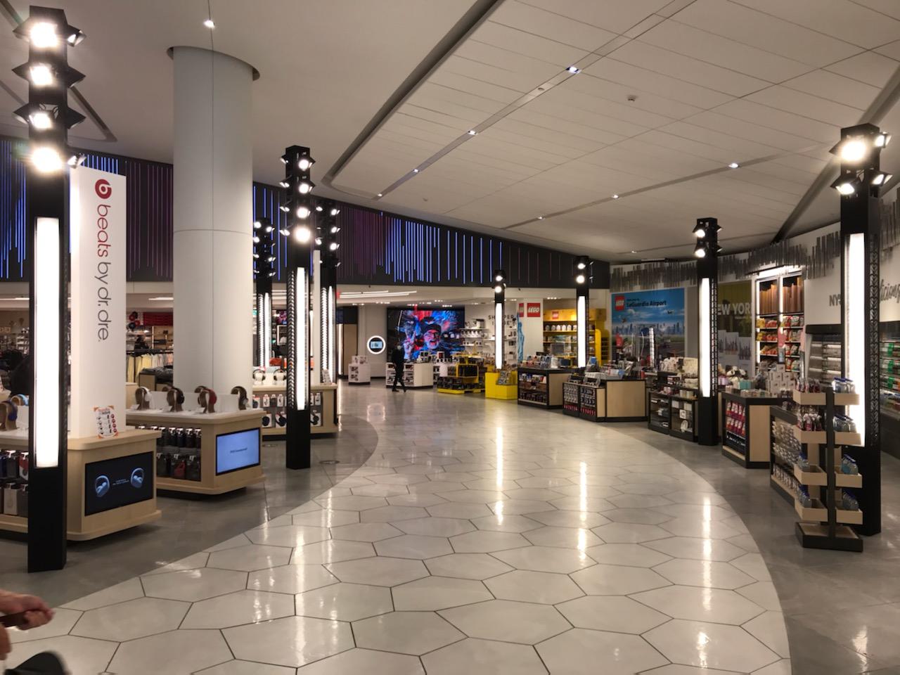 Bowery Bay Shops at LaGuardia Airport with custom lighting towers providing ambient and accent illumination along the curved retail circulation path.