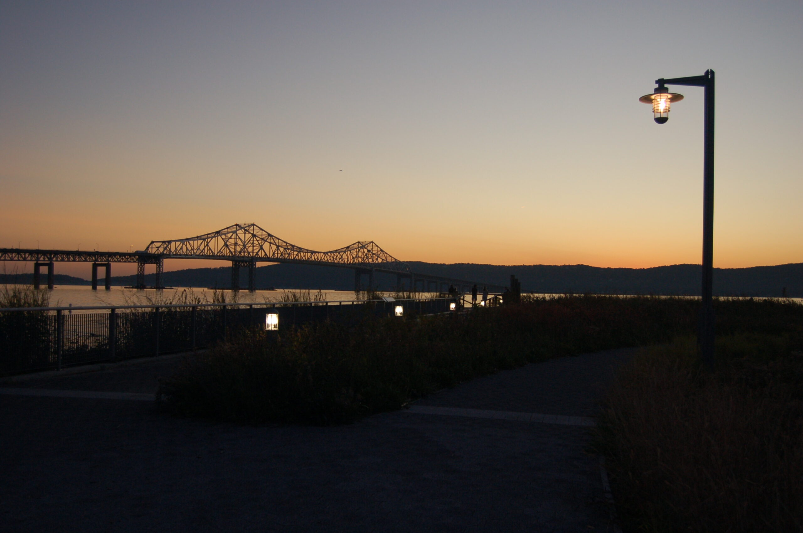 Pedestrian and bollard lighting along the Hudson River waterfront at sunset, with the Tappan Zee Bridge in the background at Hudson RiverWalk Park at Tarrytown.