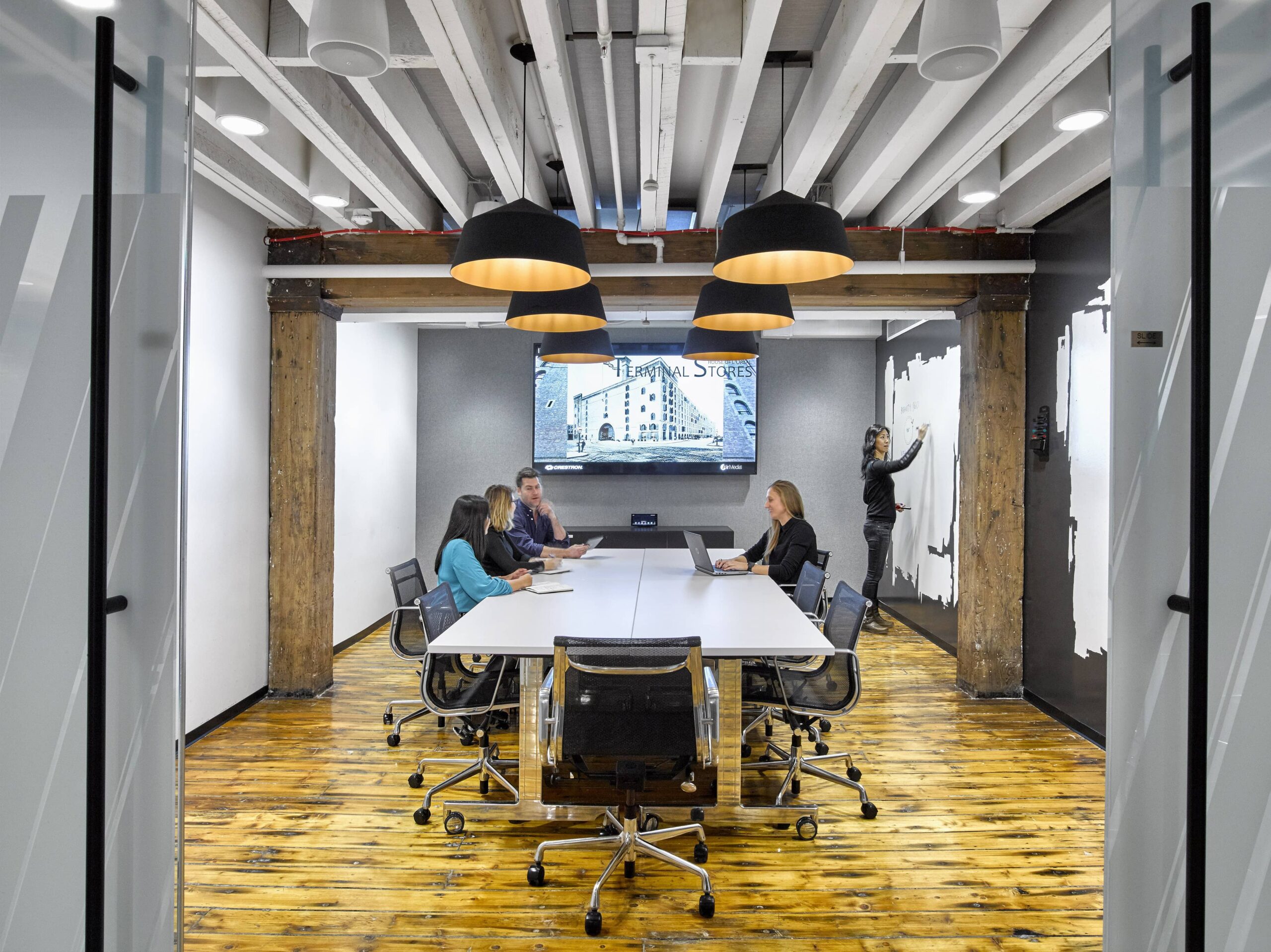 Office room with lighting pendants above conference table that has people working.