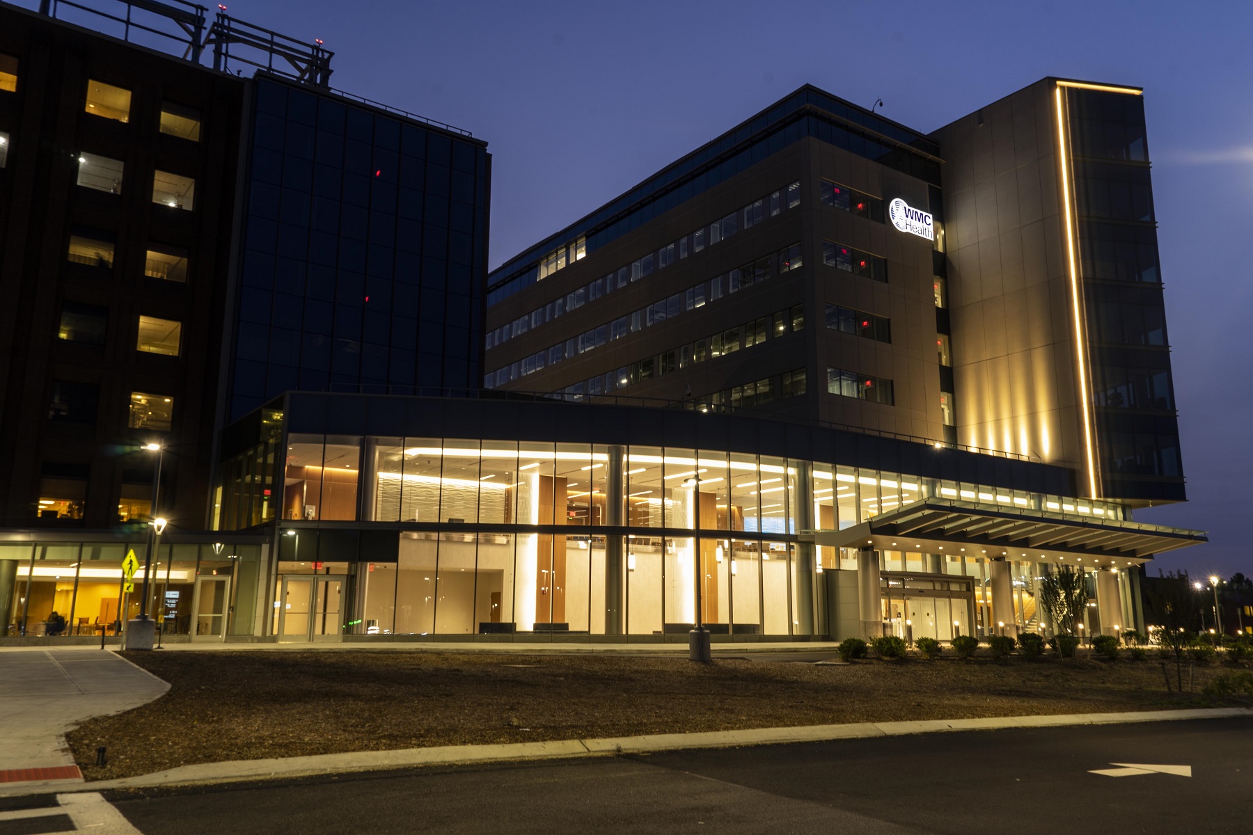 Westchester Medical Center Ambulatory Care Pavilion with illuminated glass lobby and integrated facade lighting at dusk.