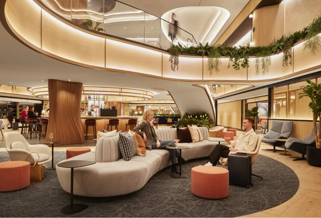 Airport lounge with layered architectural lighting integrated into curved ceilings, illuminated railings, and intimate seating areas.
