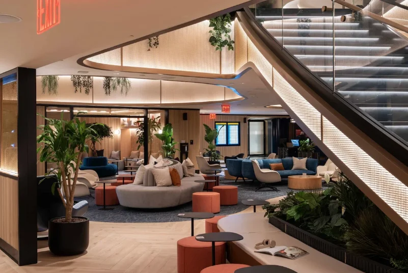 Airport lounge seating area with layered architectural lighting integrated into the staircase, curved soffits, and illuminated railings.