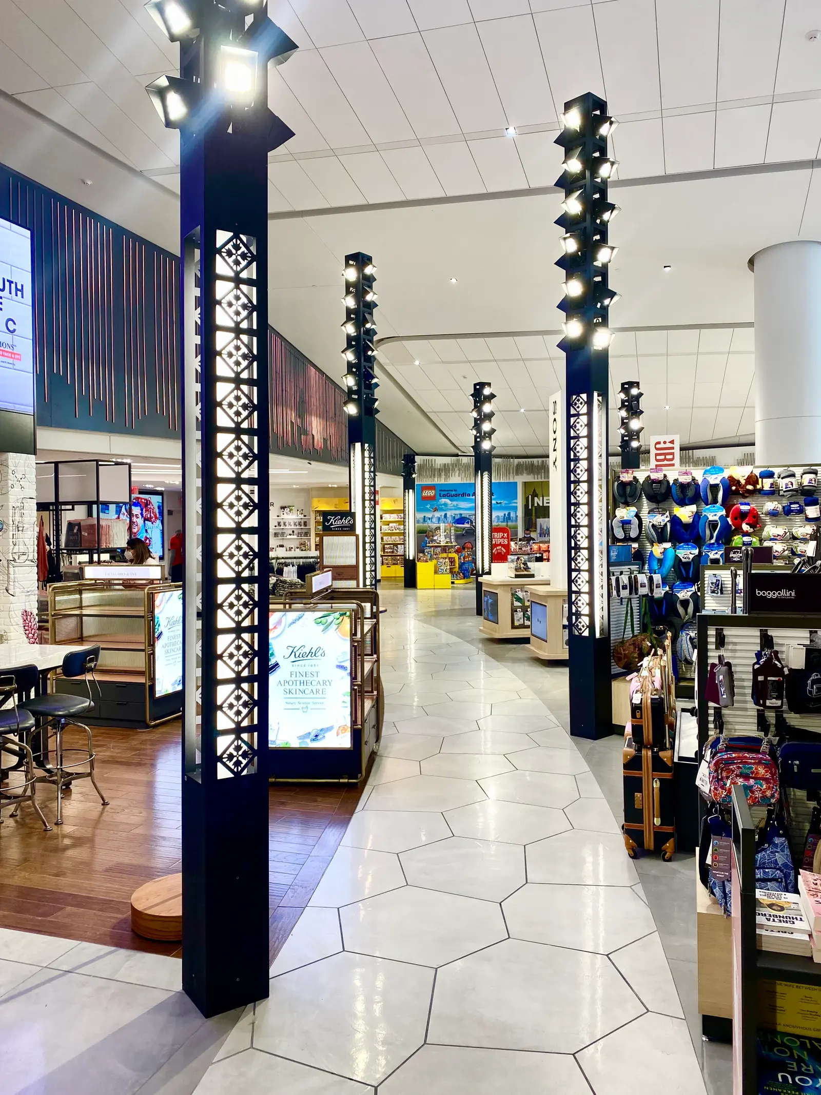 Airport retail concourse with custom light poles featuring integrated decorative panels and multiple directional lights.
