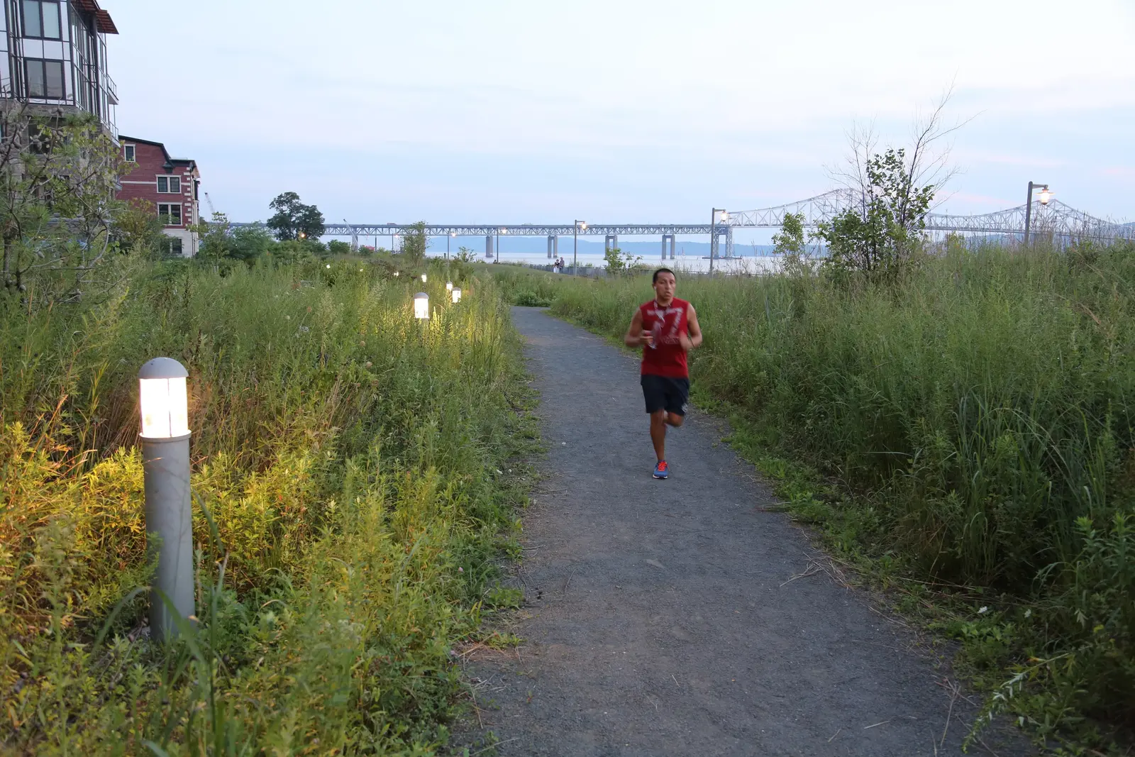 Jogger on a waterfront path illuminated by bollard lighting, with the Tappan Zee Bridge in the background at Hudson RiverWalk Park at Tarrytown.