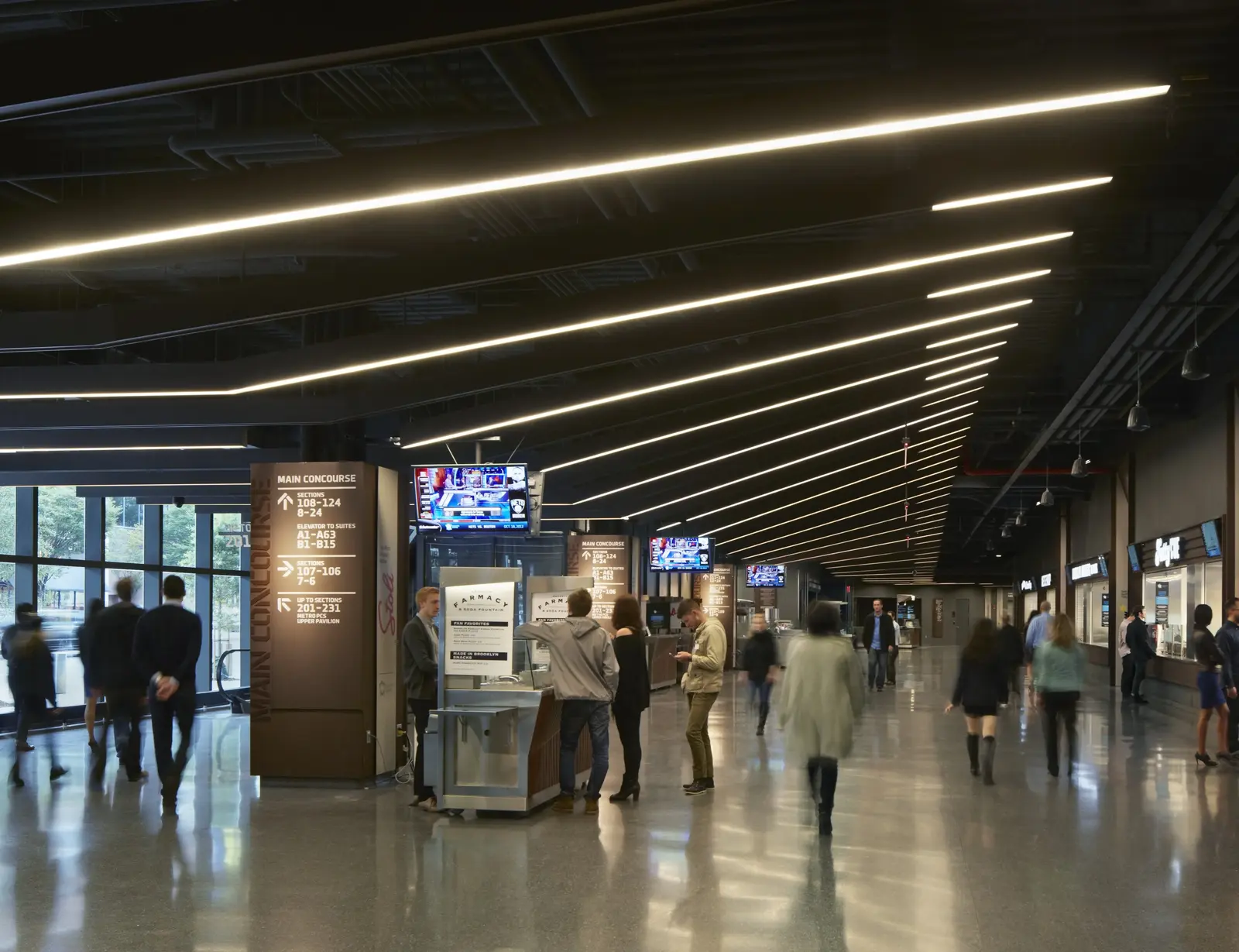 Barclays Center main concourse with custom linear lighting fixtures integrated into the angled Corten steel beams of the ceiling.