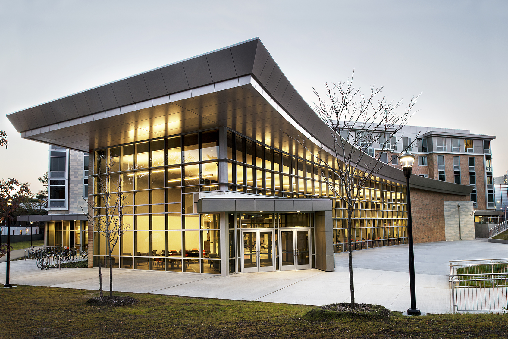 SUNY Stony Brook University East Side Dining exterior at dusk with illuminated glass facade and welcoming interior light.